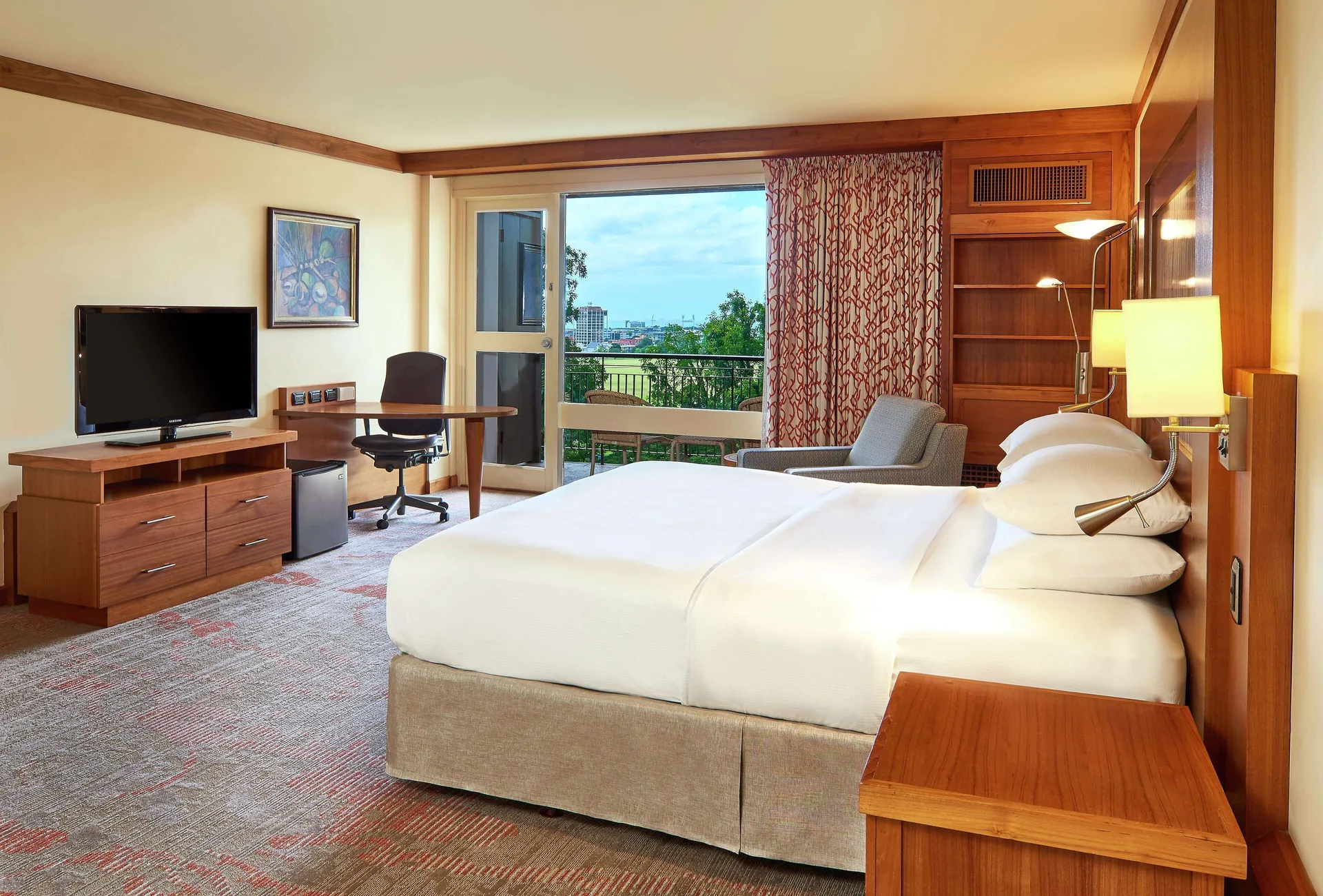 Room Garden View with king bed, balcony, TV, and desk at Hilton Trinidad and Conference Centre with hillside views.