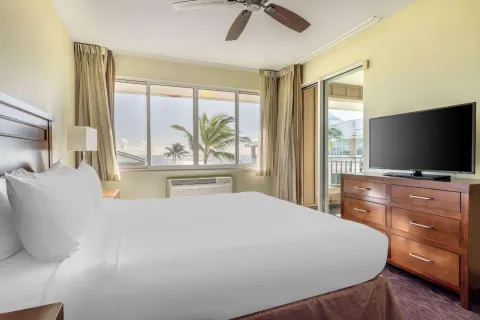 Guest room with king bed, dresser, TV, and balcony at Hilton Vacation Club The Point At Poipu Kauai.