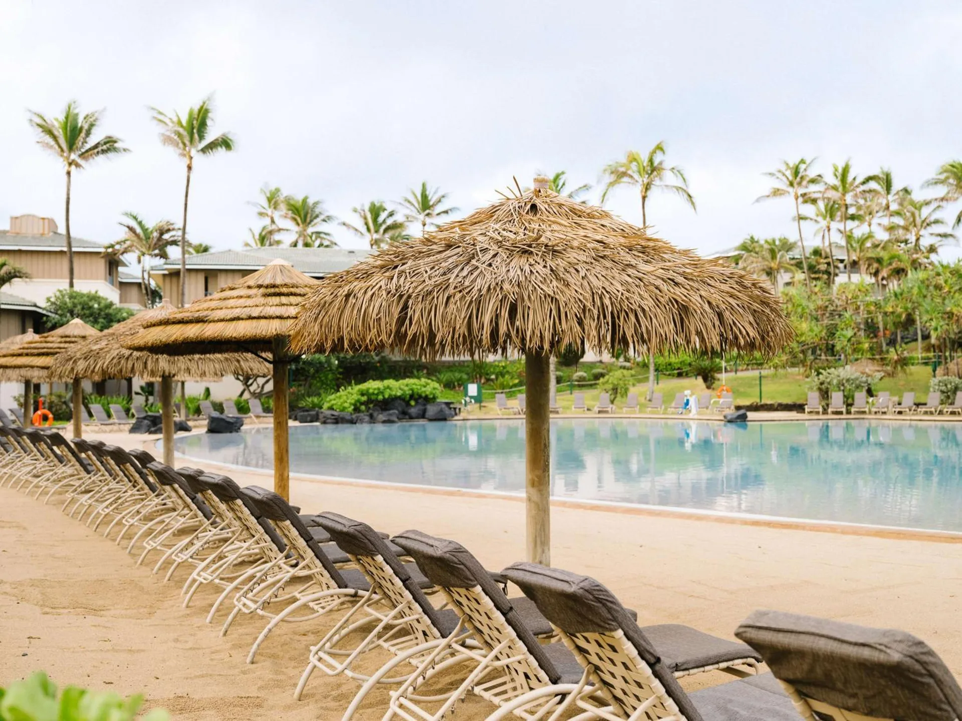 Poolside lounge chairs and thatched umbrellas at Hilton Vacation Club The Point At Poipu Kauai.