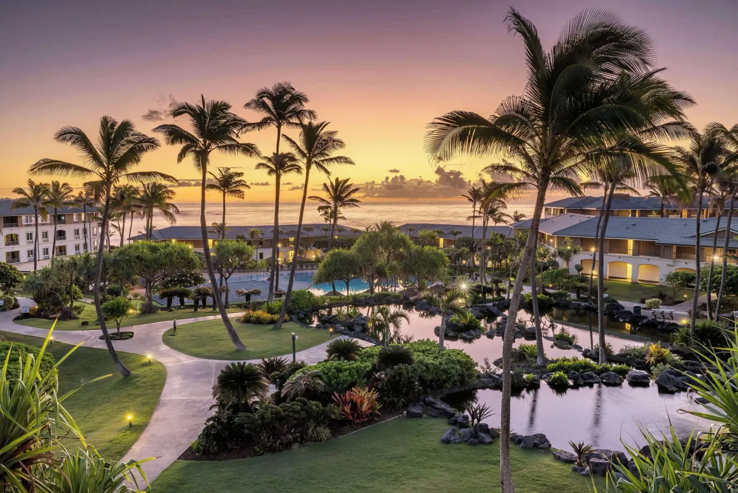 Sunset over palm-lined lagoons and resort buildings at Hilton Vacation Club The Point At Poipu Kauai.