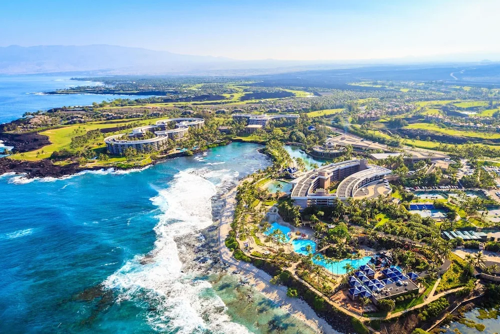 Aerial view of Hilton Waikoloa Village along the rocky coastline with pools, lagoons, and ocean surf.