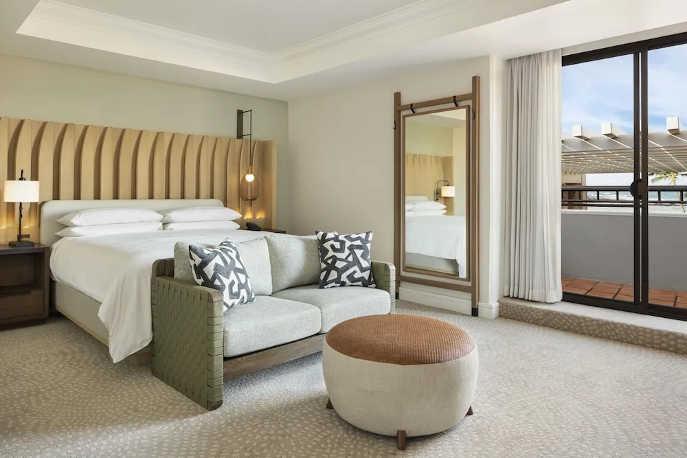 King guest room with loveseat, ottoman, mirror and balcony at Hilton Waikoloa Village.
