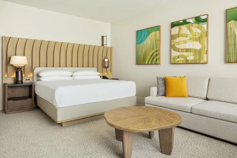 King guest room with sofa, round table and tropical artwork at Hilton Waikoloa Village.