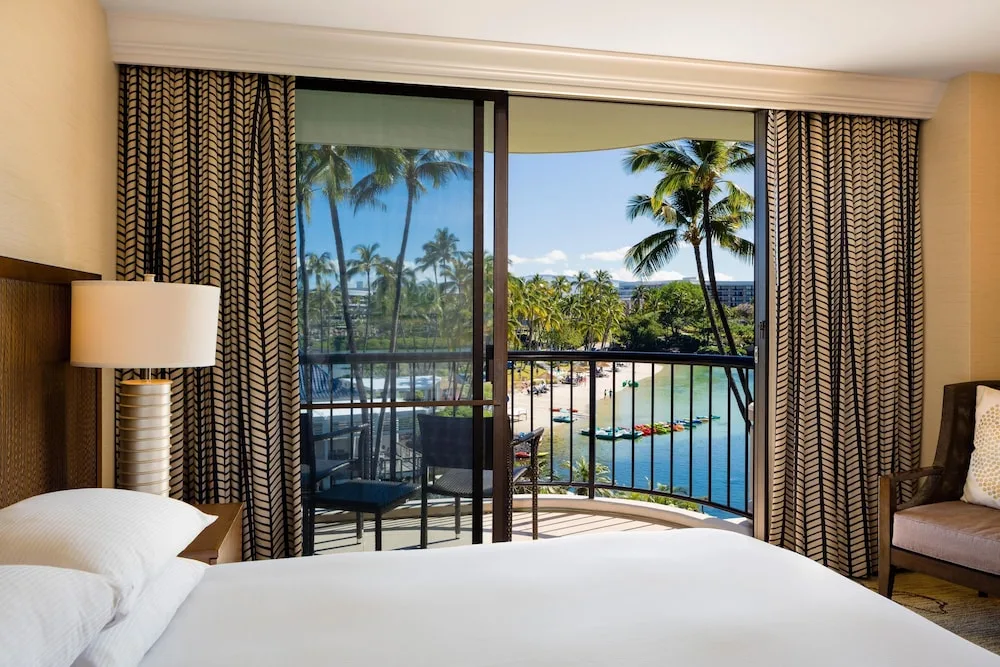 King bed beside a balcony with lagoon and palm views at Hilton Waikoloa Village.