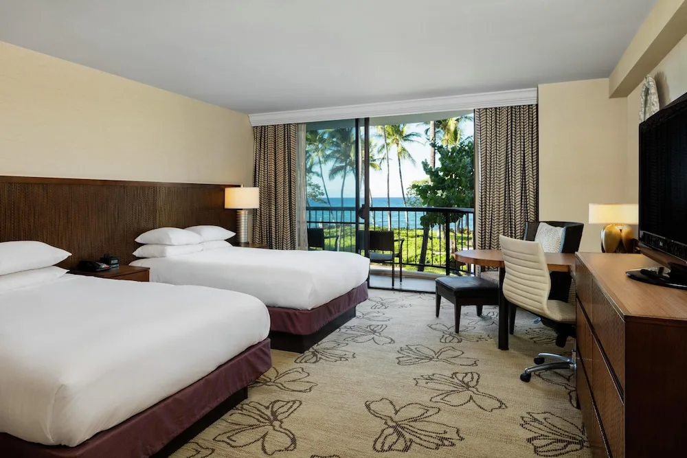 Two-bed guest room with ocean view balcony and work desk at Hilton Waikoloa Village.