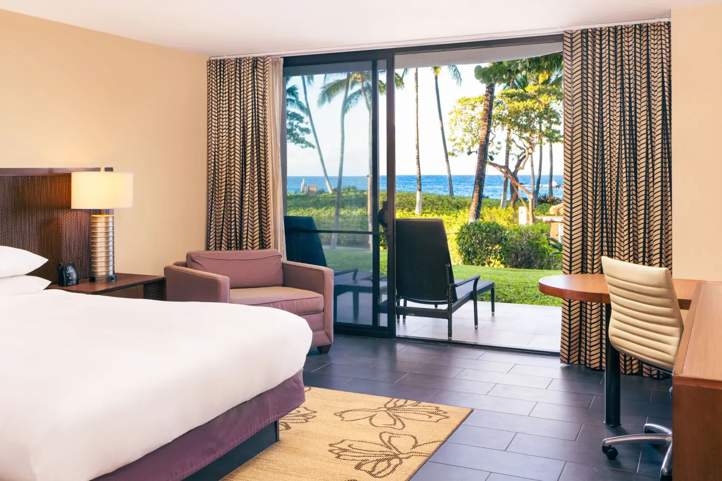 King bed guest room with patio and ocean beyond at Hilton Waikoloa Village.