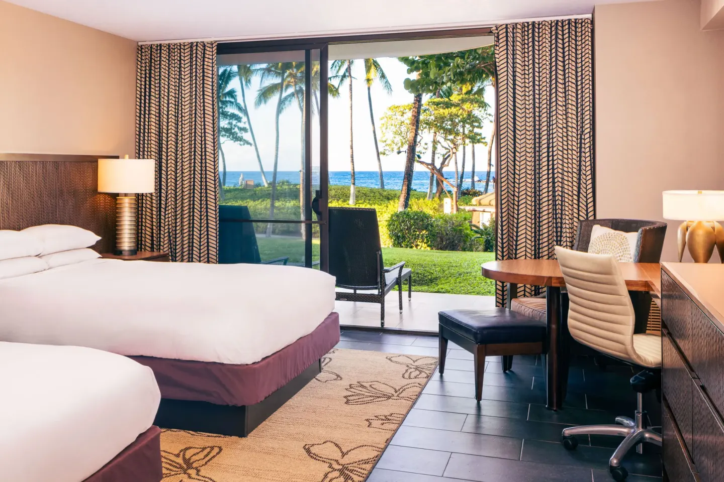 Two-bed guest room with patio facing palms and ocean at Hilton Waikoloa Village.