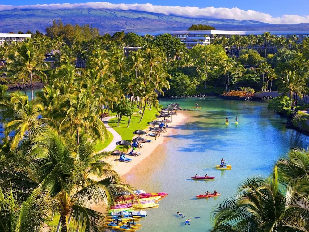 Saltwater lagoon with kayaks, beach chairs, and palms at Hilton Waikoloa Village.