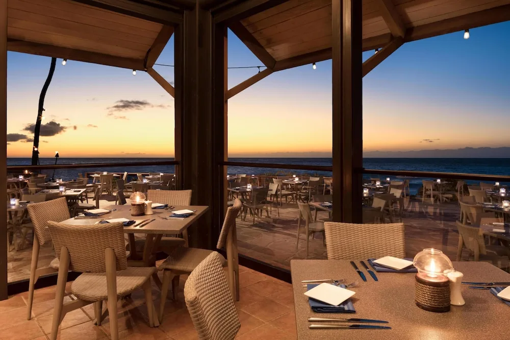 Oceanfront dining room at sunset with candlelit tables at Hilton Waikoloa Village.
