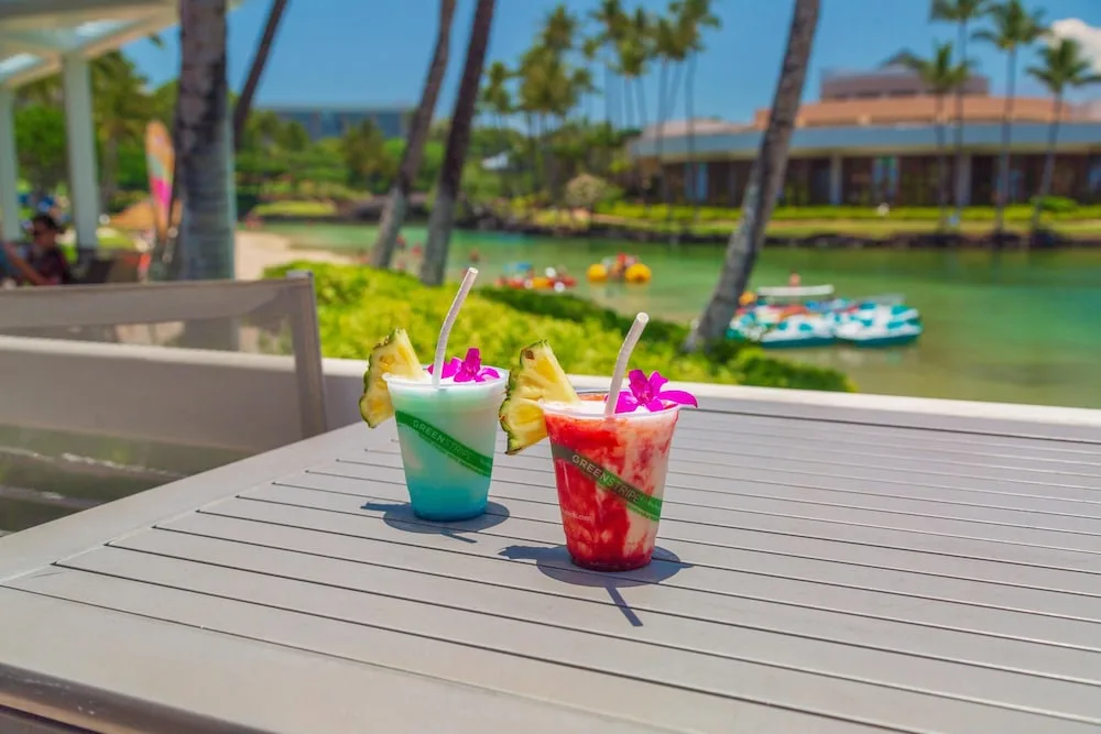 Two tropical frozen drinks on an outdoor table by the lagoon at Hilton Waikoloa Village.