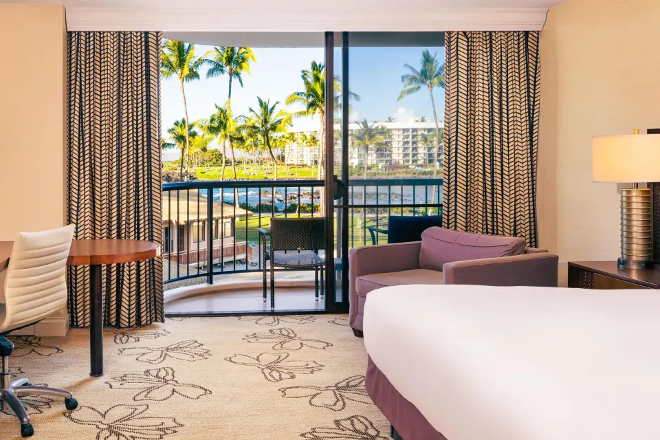 Makai oceanfront room with bed, desk, sofa, and balcony at Hilton Waikoloa Village.
