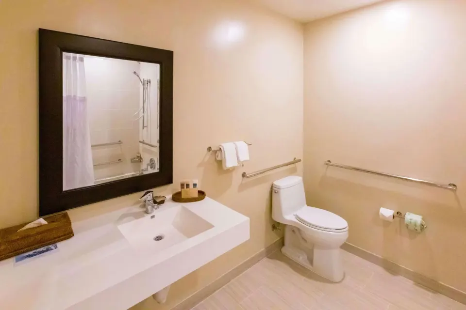 Accessible bathroom with sink, toilet, grab bars, and shower mirror view at Hilton Waikoloa Village.