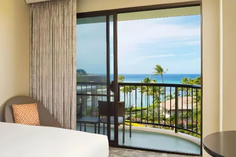 Balcony ocean view from a guest room with bed edge and chair at Hilton Waikoloa Village.