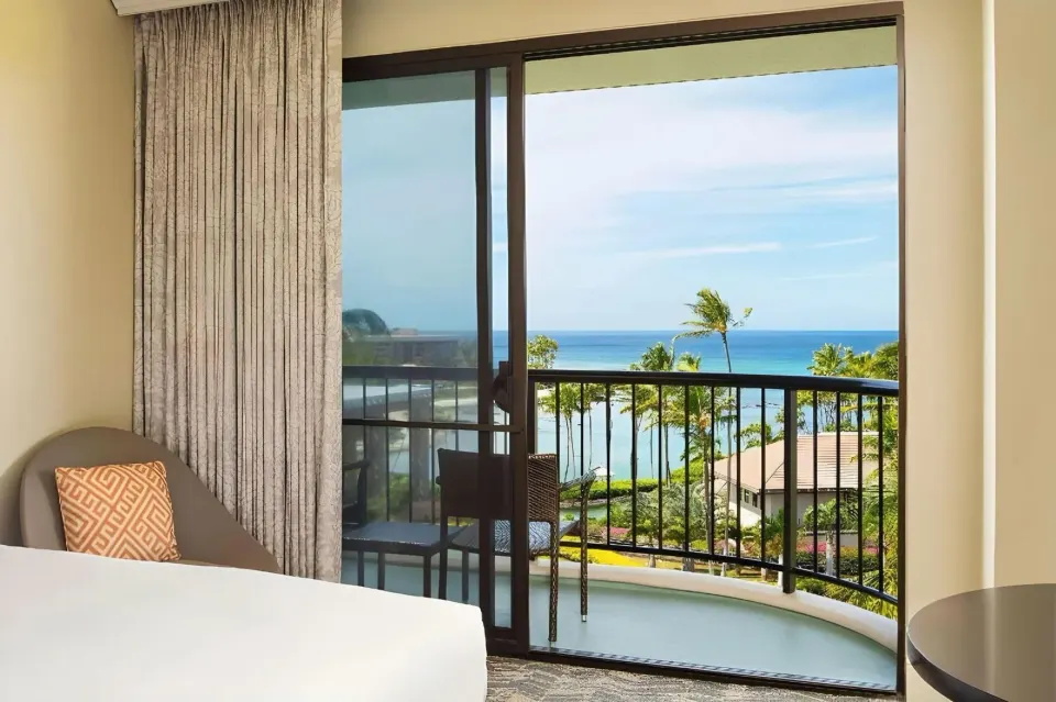 Balcony ocean view from a guest room with bed edge and chair at Hilton Waikoloa Village.