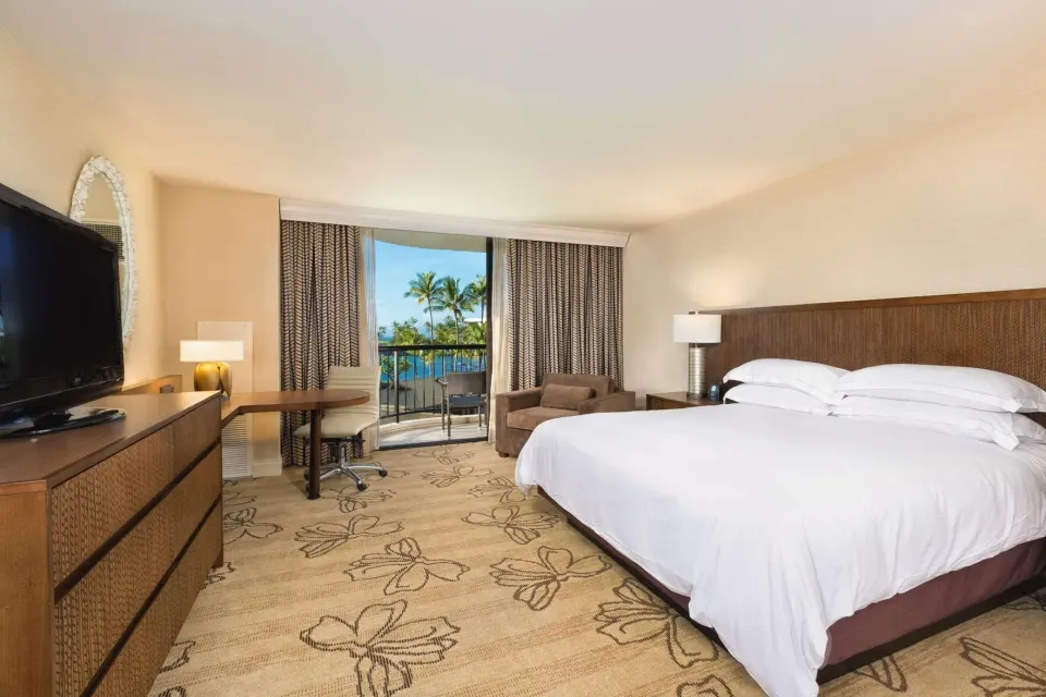 Ocean view king room with balcony, desk, TV, and seating at Hilton Waikoloa Village.