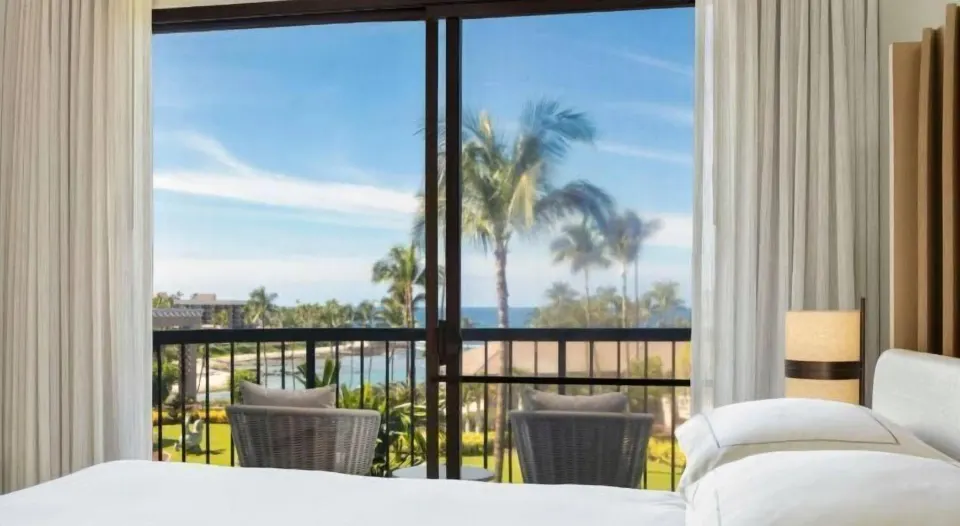 Ocean view from a guest room bed to balcony chairs at Hilton Waikoloa Village.