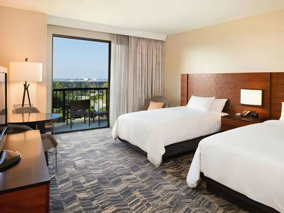 Ocean view room with two beds, desk, balcony, and wood headboard at Hilton Waikoloa Village.