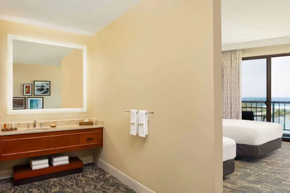 Guest room vanity and bedroom area with balcony view at Hilton Waikoloa Village.