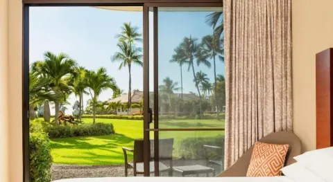 Guest room sliding door opens to lawn and palm views at Hilton Waikoloa Village.