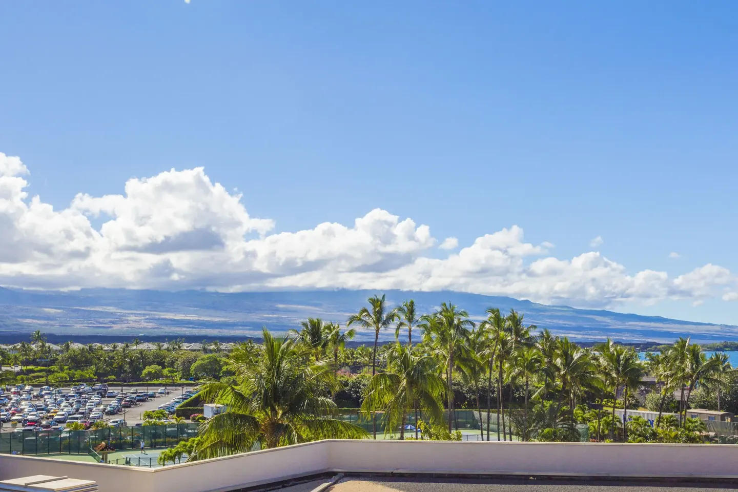 Resort view from Hilton Waikoloa Village with palms, courts, parking, ocean and mountains.