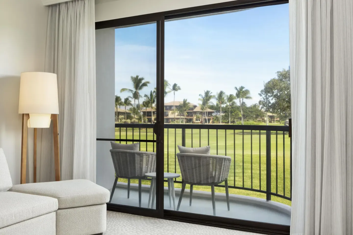 Balcony seating and resort lawn view from a guest room at Hilton Waikoloa Village.
