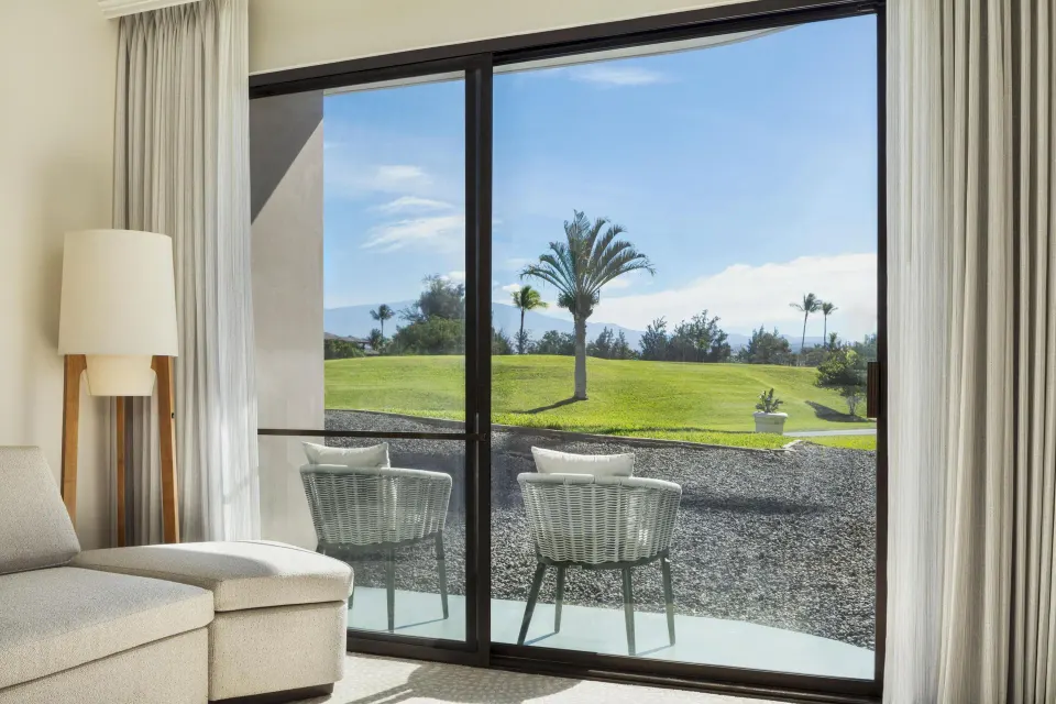 Ground-level patio chairs facing a palm and lawn view at Hilton Waikoloa Village.
