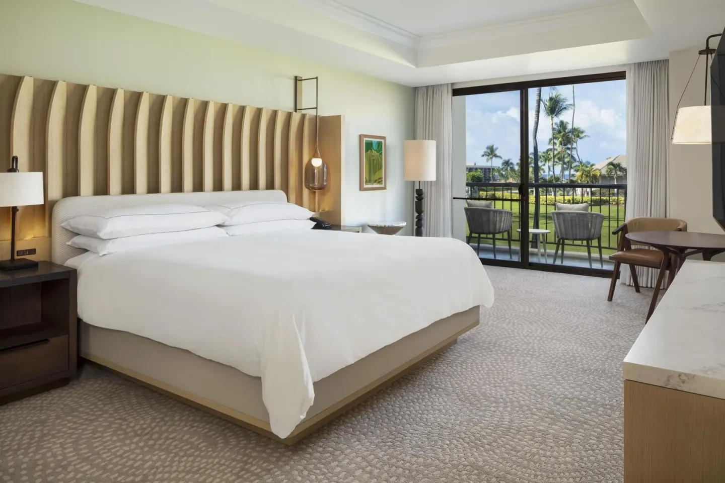 King bedroom with balcony seating and resort grounds view at Hilton Waikoloa Village.