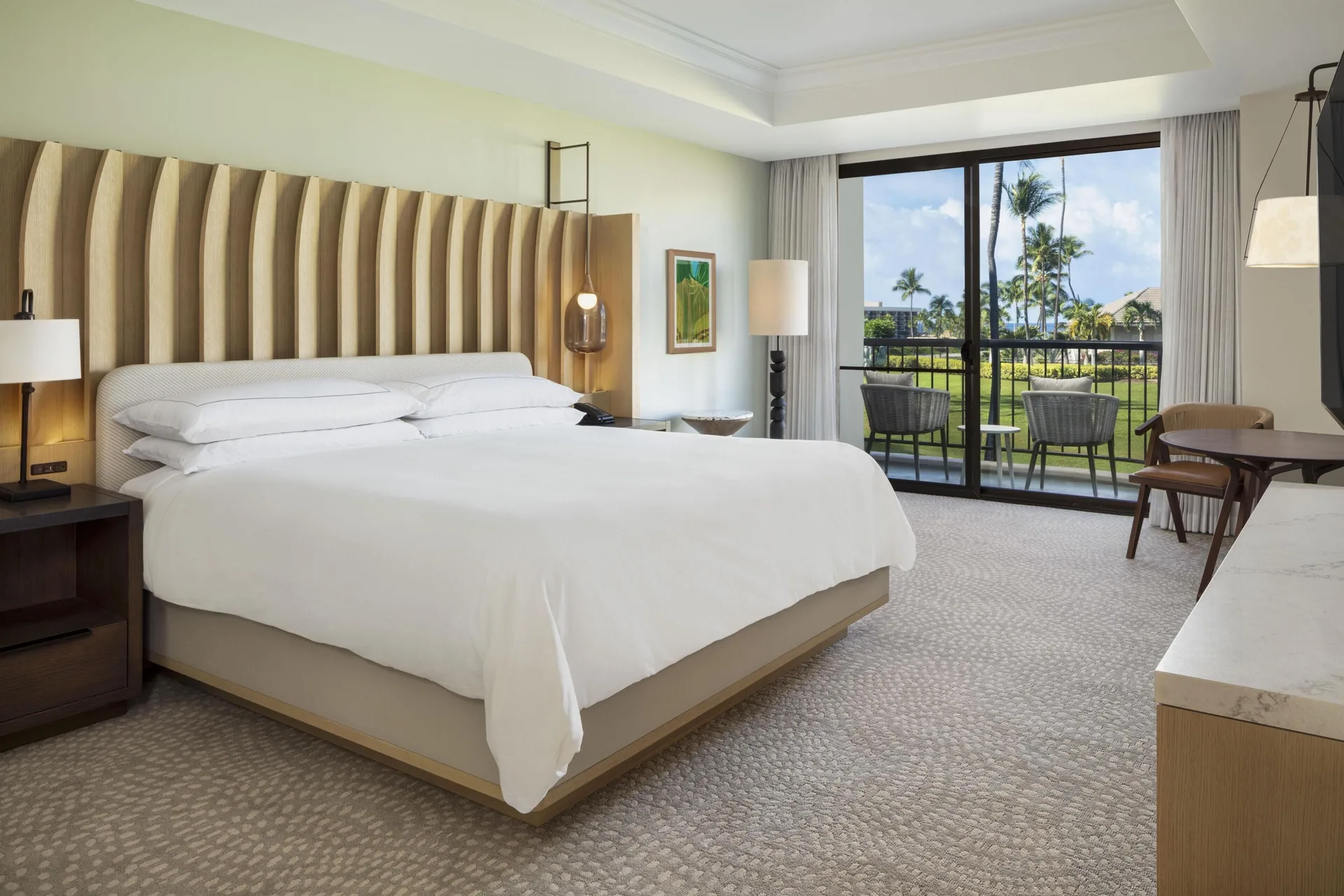 King bedroom with balcony seating and resort grounds view at Hilton Waikoloa Village.