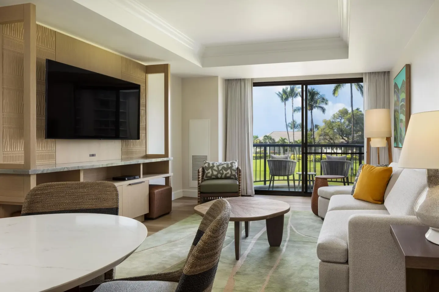 Suite living room with sofa, TV, dining table, and balcony at Hilton Waikoloa Village.