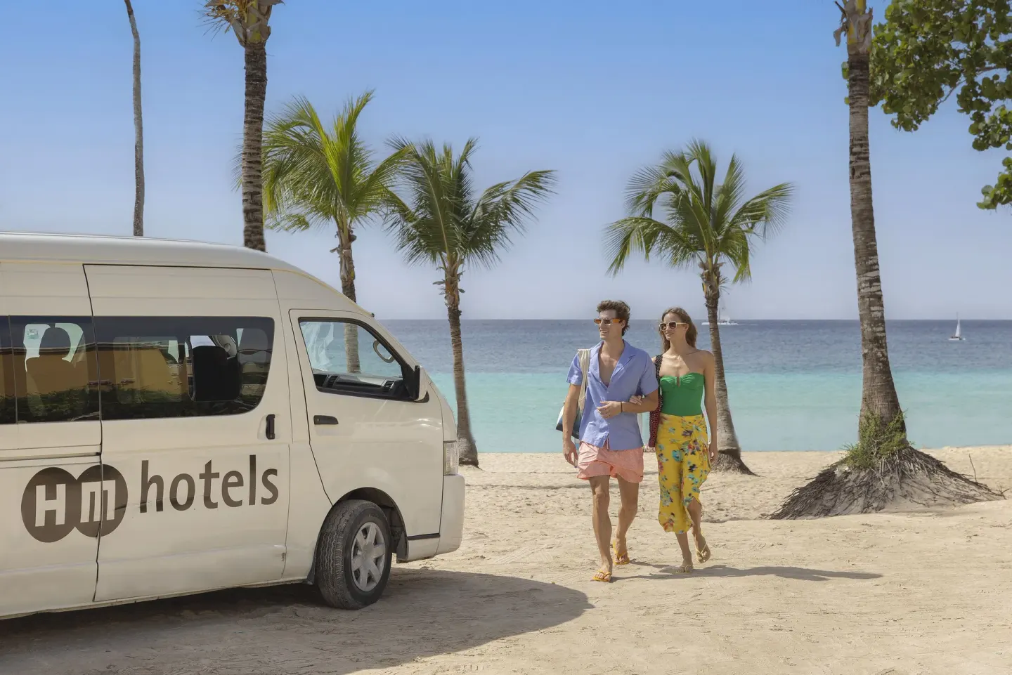 Guests walking beside an HM hotels van on a palm-lined beach at HM Alma de Bayahibe.