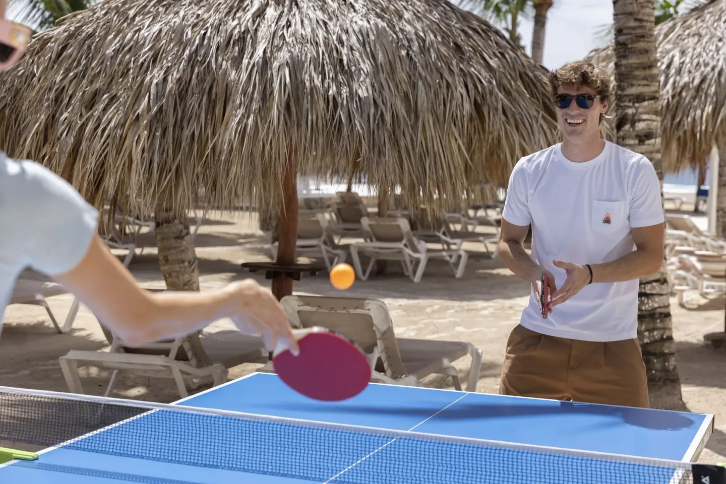 Guests play table tennis by thatched shade and lounge chairs at HM Alma de Bayahibe.