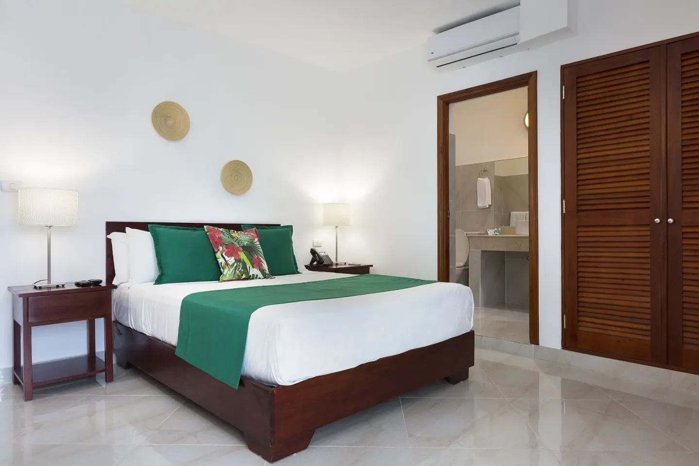 Guest room with king bed, open bathroom doorway and wood closet at HM Alma de Bayahibe.