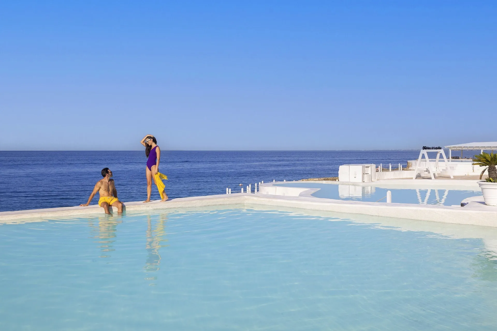 Guests stand at the edge of an infinity-style pool facing the sea at HM Alma de Bayahibe.