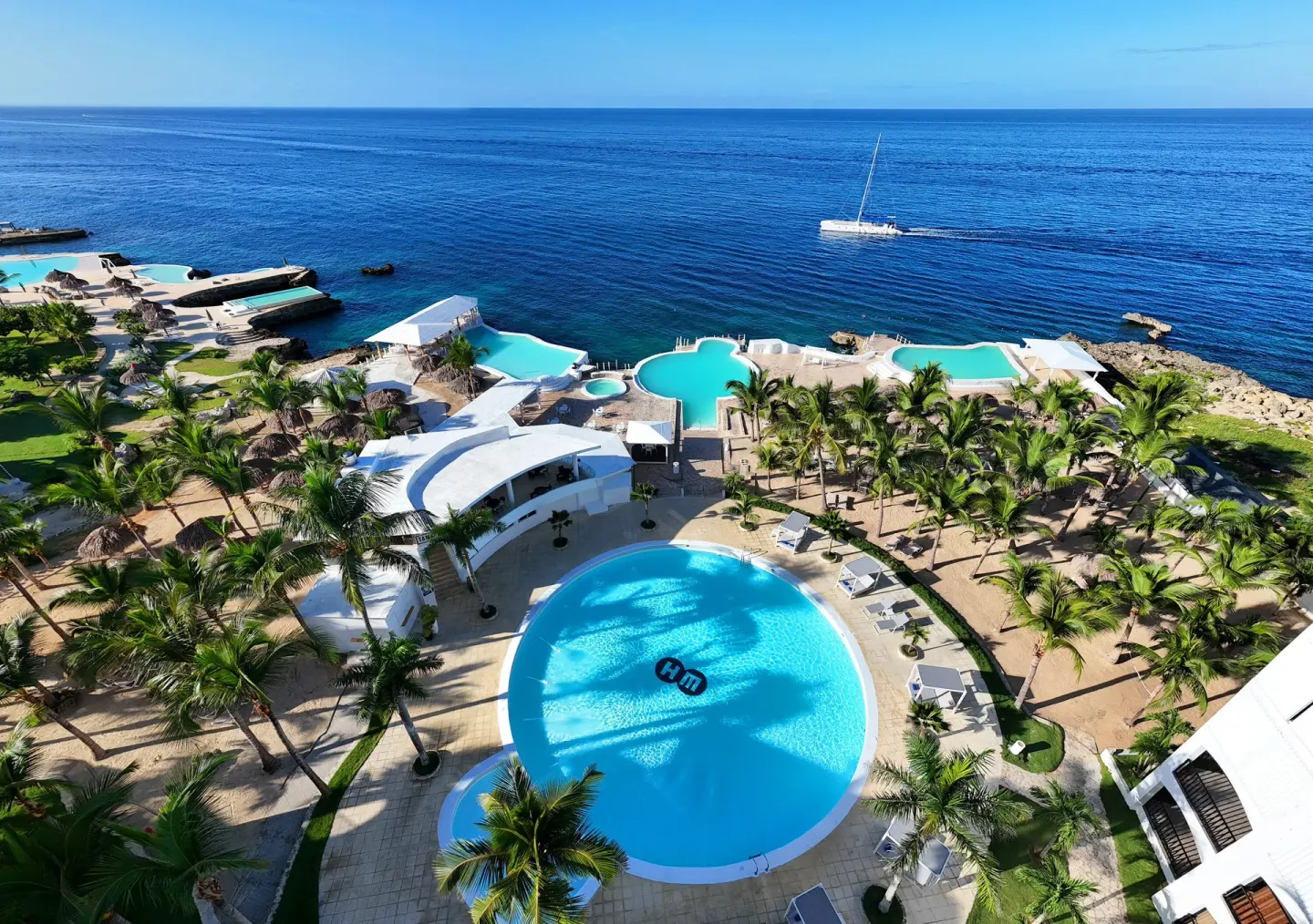 Aerial view of oceanfront pools and palms at HM Alma de Bayahibe.