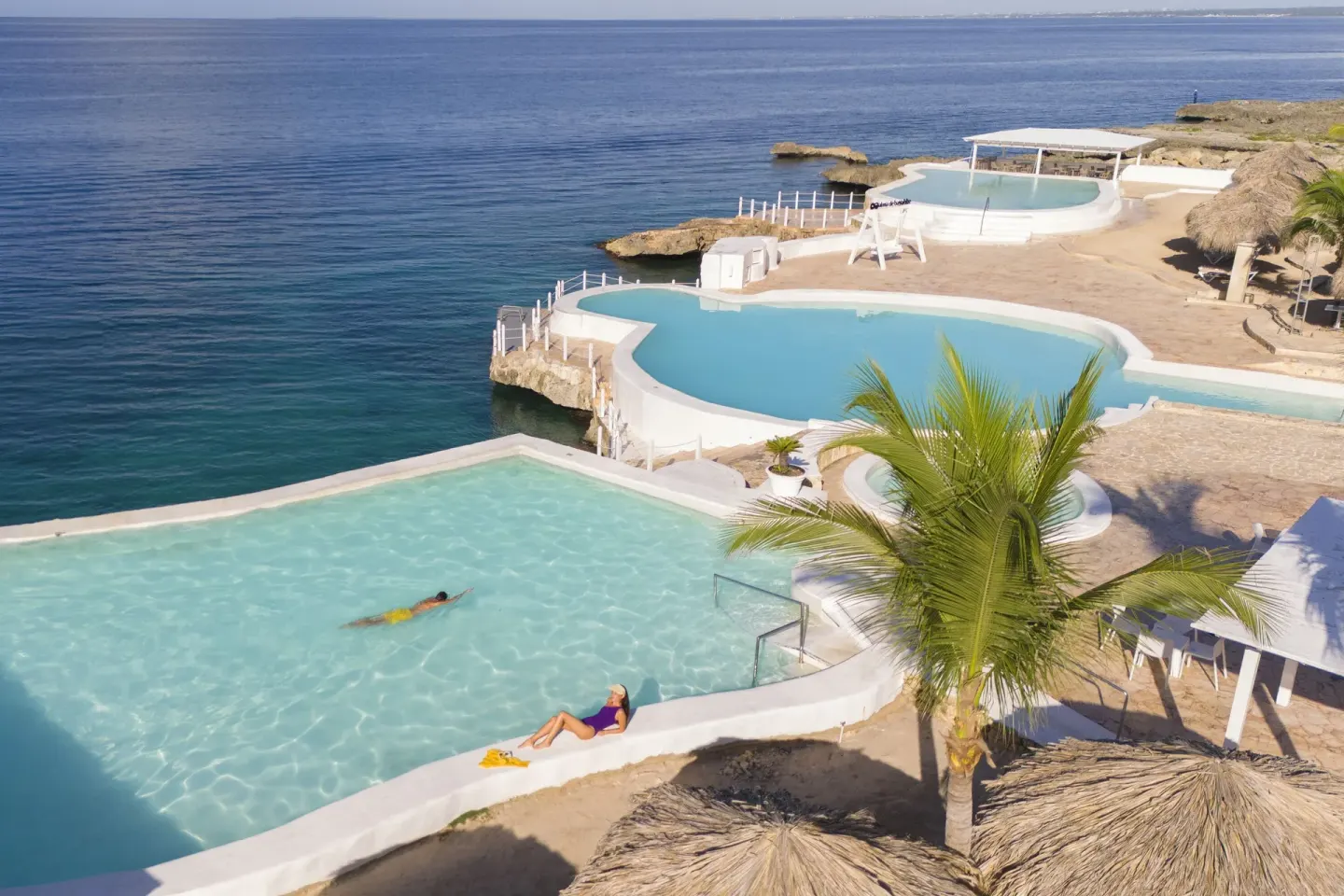 Aerial view of oceanfront pools and rocky shoreline at HM Alma de Bayahibe.