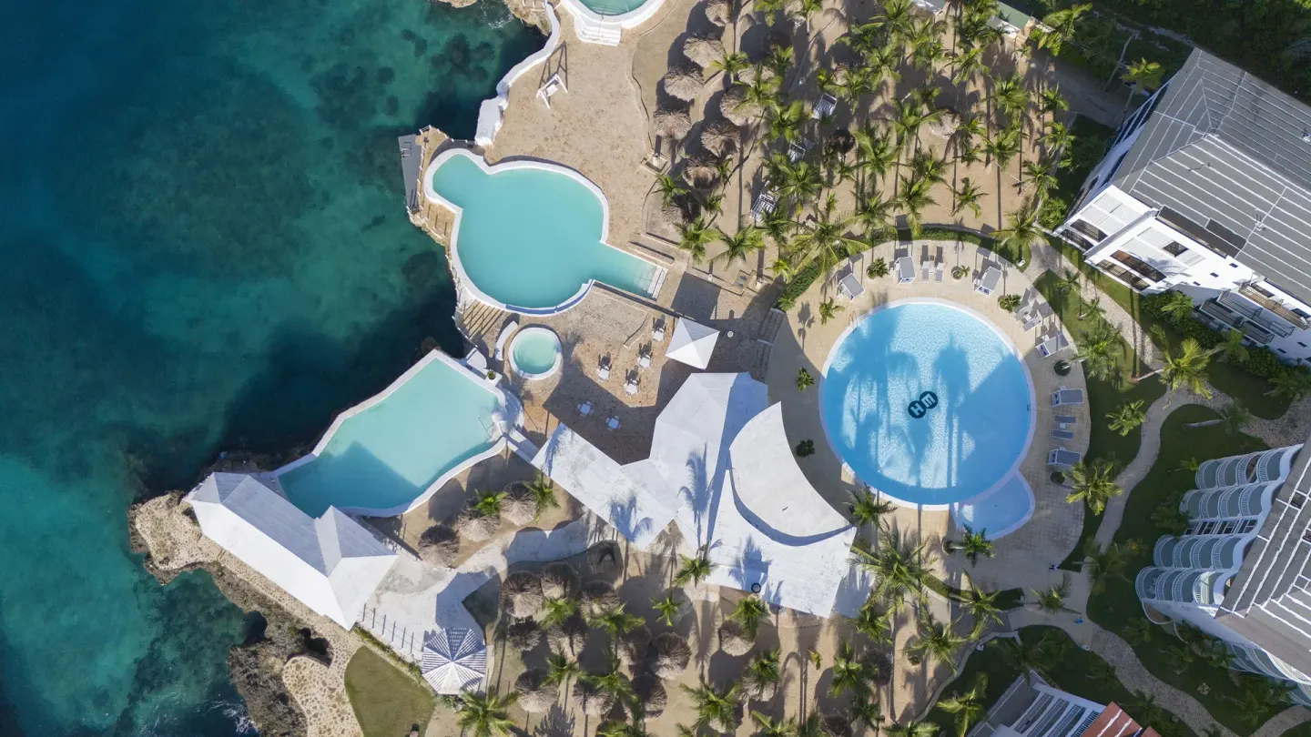 Overhead view of connected seaside pools and palm areas at HM Alma de Bayahibe.