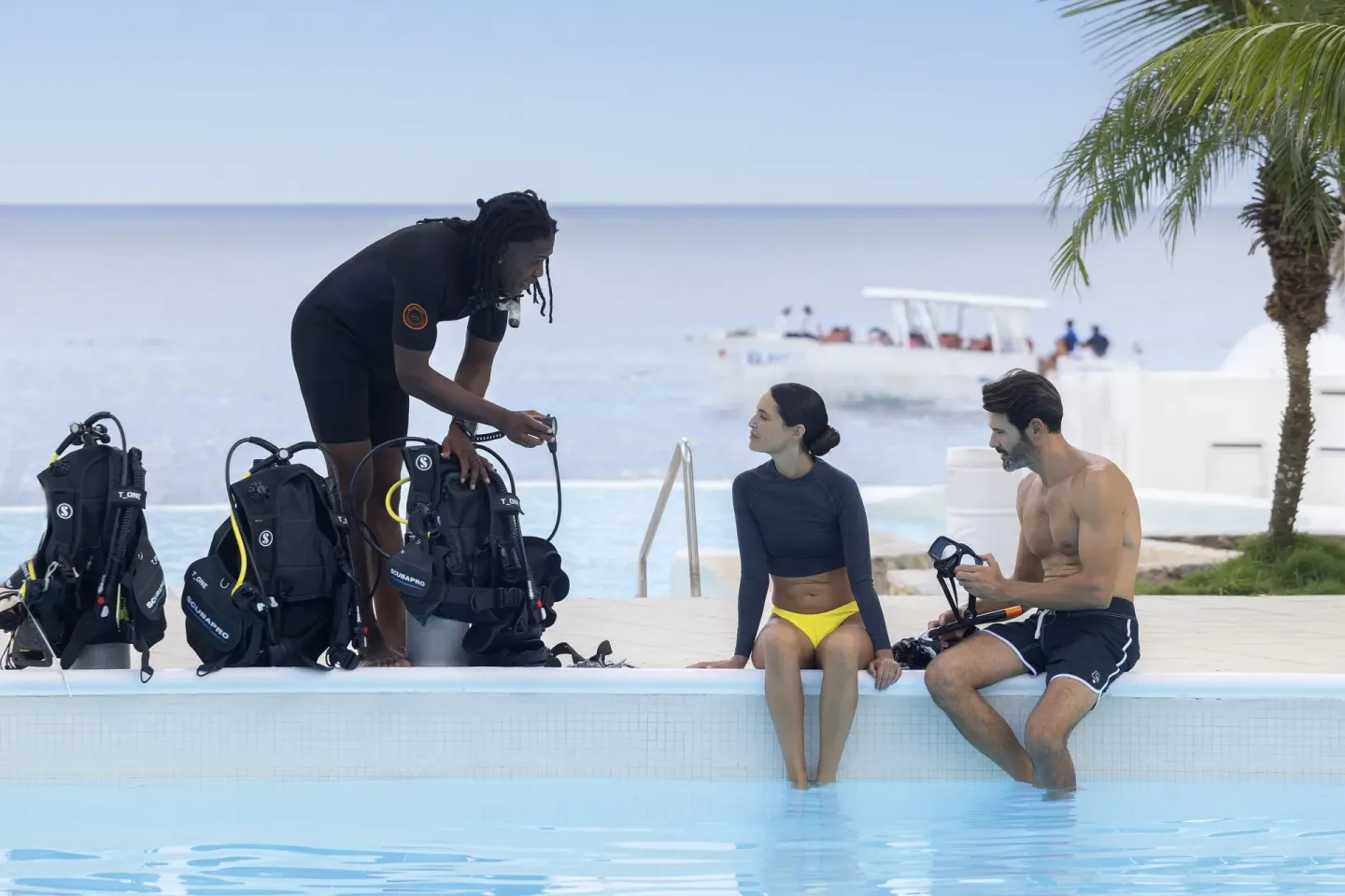 Guests sit by the pool with scuba gear and an instructor at HM Alma de Bayahibe.