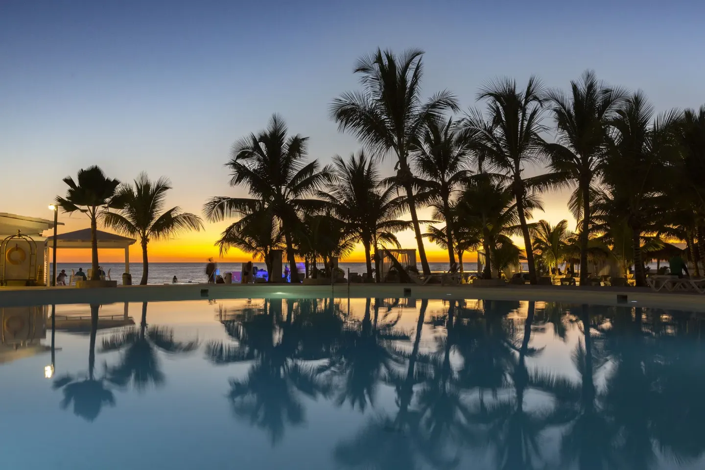 Pool reflecting palm silhouettes at sunset by the ocean at HM Alma de Bayahibe.