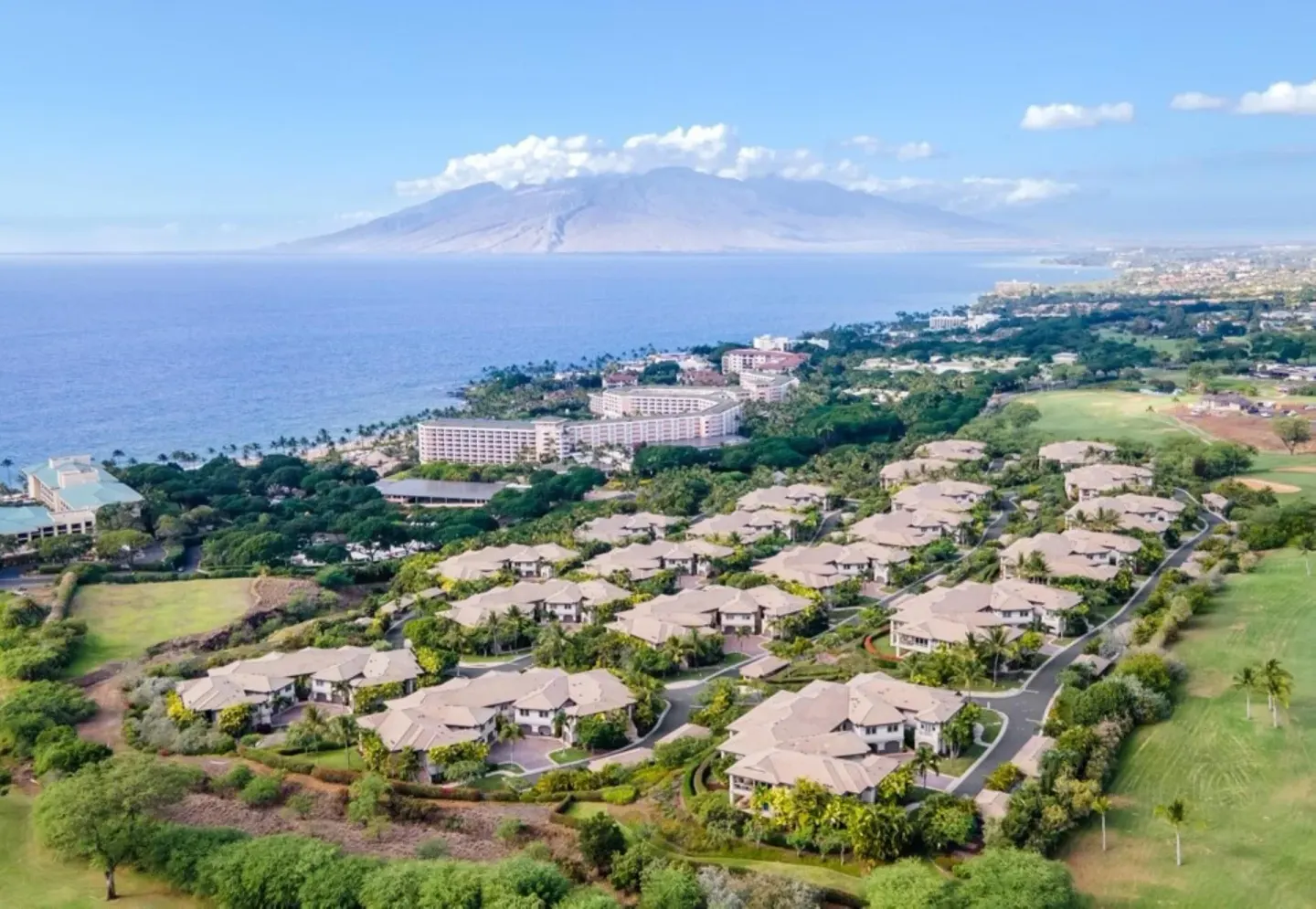 Wide aerial view of Ho‘olei Villas at Grand Wailea near the coast with ocean and mountains beyond.