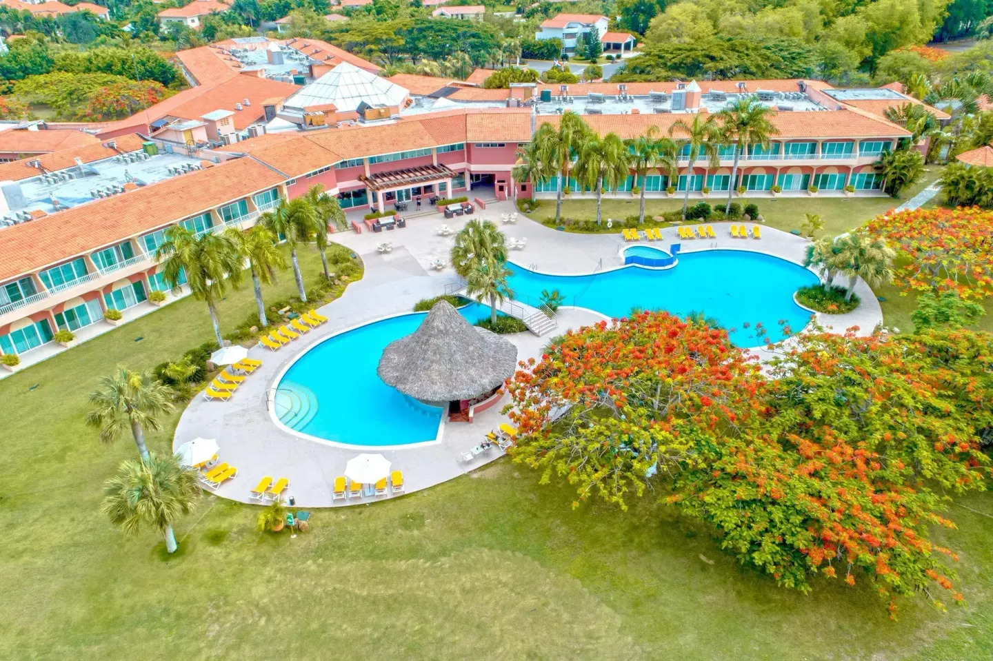 Aerial view of pools, palms, and resort buildings at Hodelpa Garden Suites Golf & Convention Center.