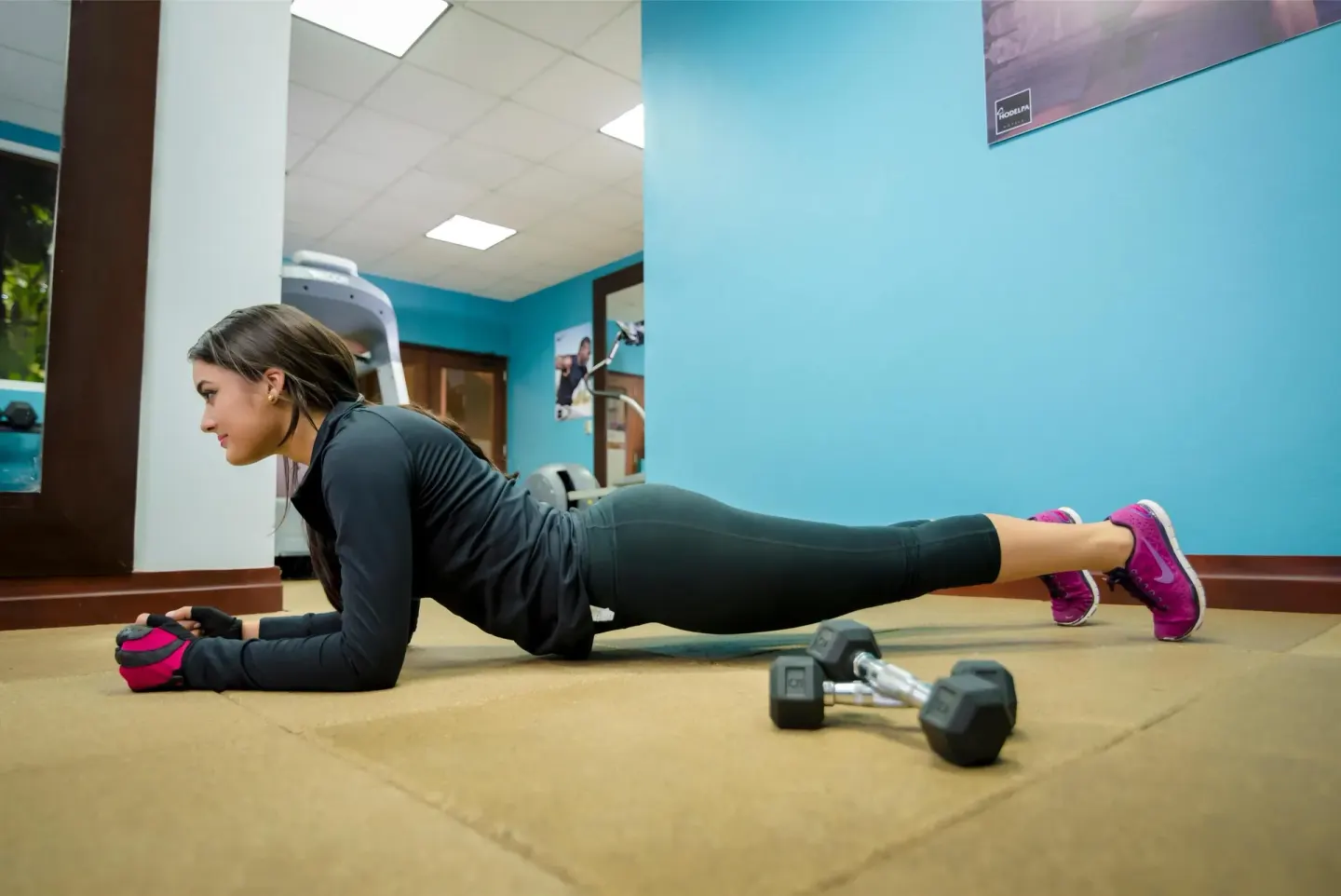 A guest holds a plank beside dumbbells in the gym at Hodelpa Garden Suites Golf & Convention Center.