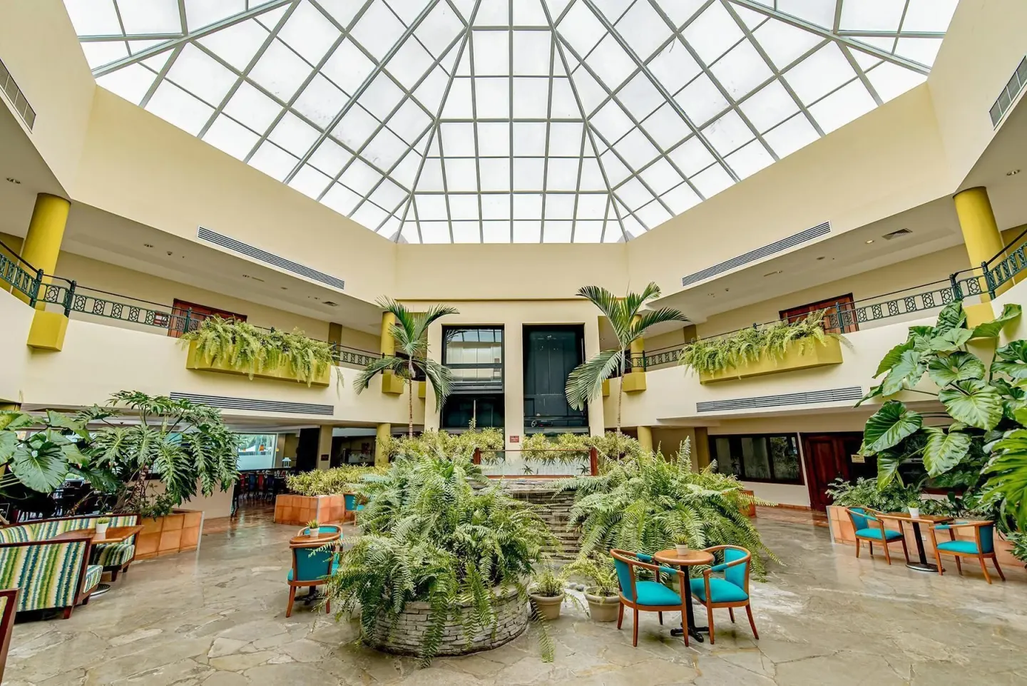 Plant-filled atrium with glass roof at Hodelpa Garden Suites Golf & Convention Center.