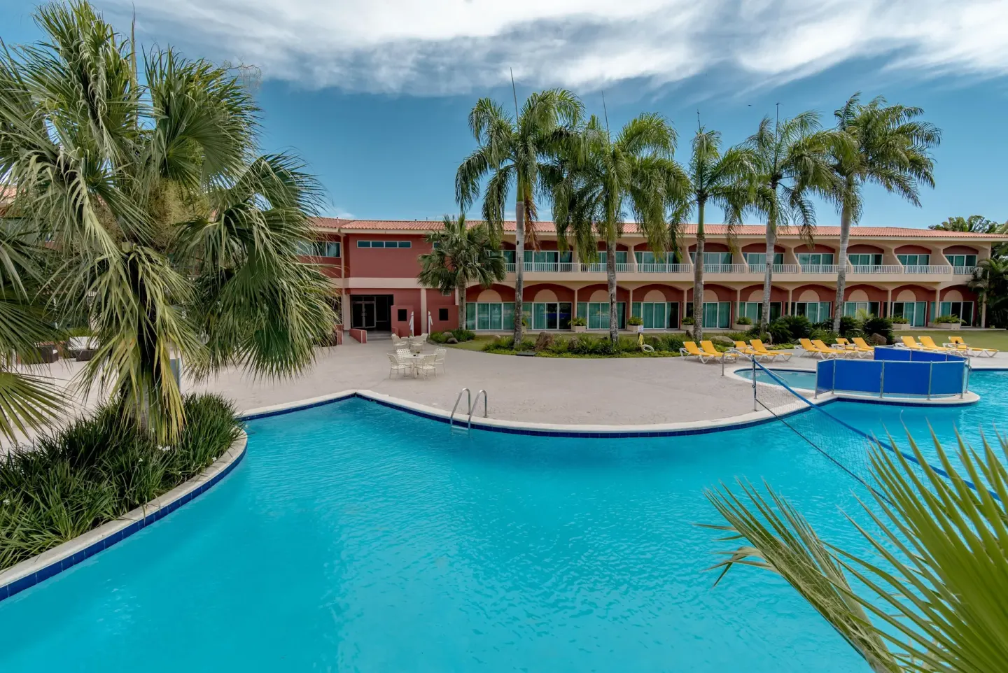 Pool, palm trees, and pink guestroom building at Hodelpa Garden Suites Golf & Convention Center.