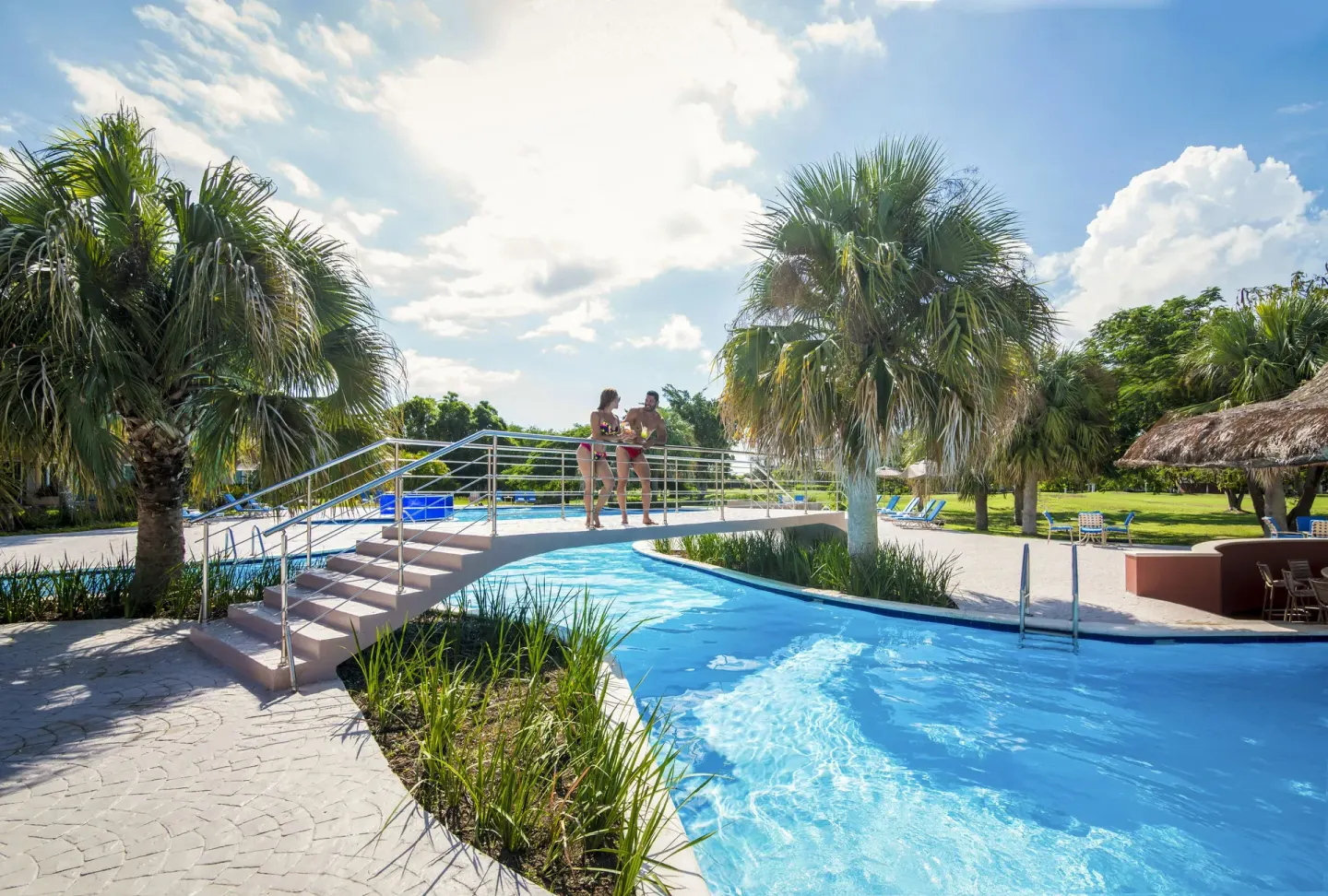 Footbridge over the resort pool with palms at Hodelpa Garden Suites Golf & Convention Center.