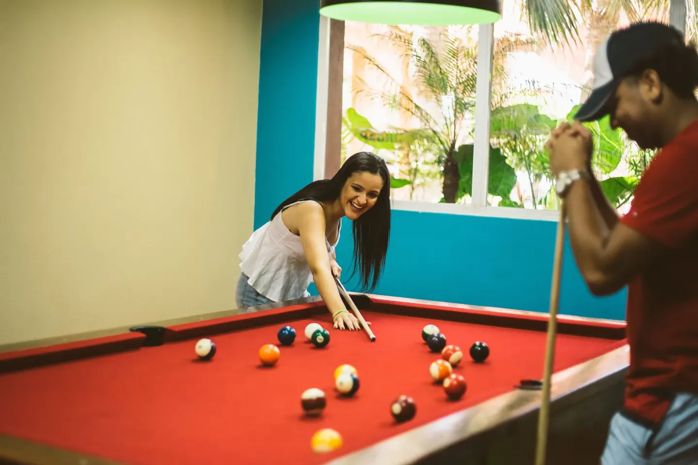 Two guests play pool beside large windows at Hodelpa Garden Suites Golf & Convention Center.