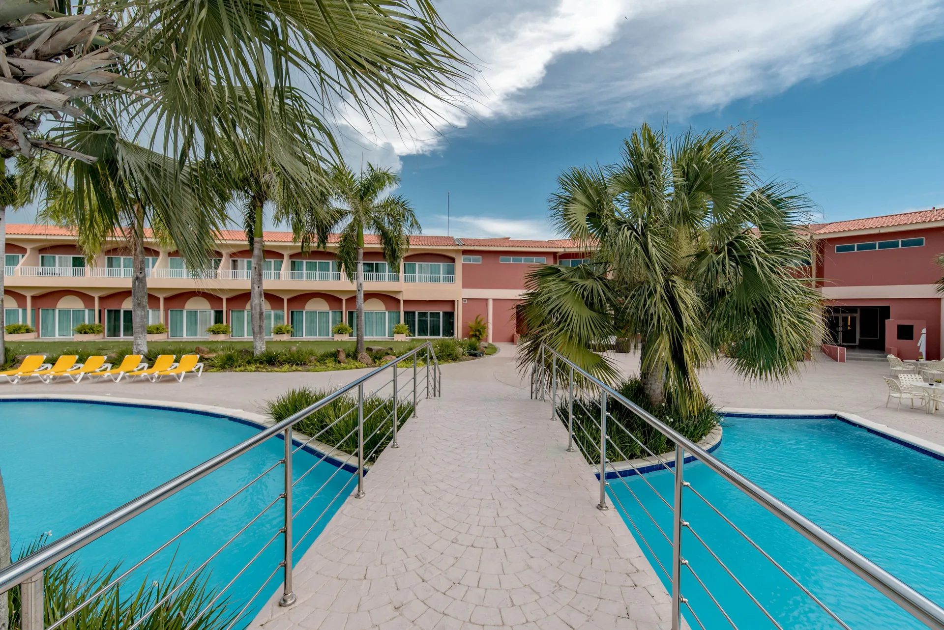 Pool walkway between palm trees at Hodelpa Garden Suites Golf & Convention Center.