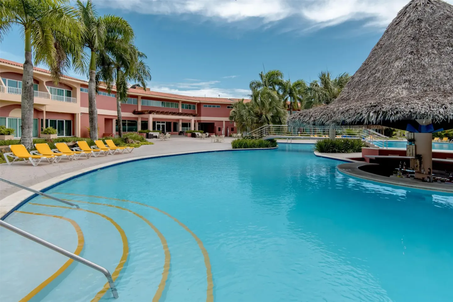 Pool with thatched swim-up bar area at Hodelpa Garden Suites Golf & Convention Center.