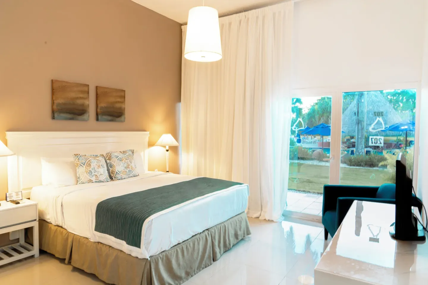 Family Suite king bed, TV, and patio doors at Hodelpa Garden Suites Golf & Convention Center.