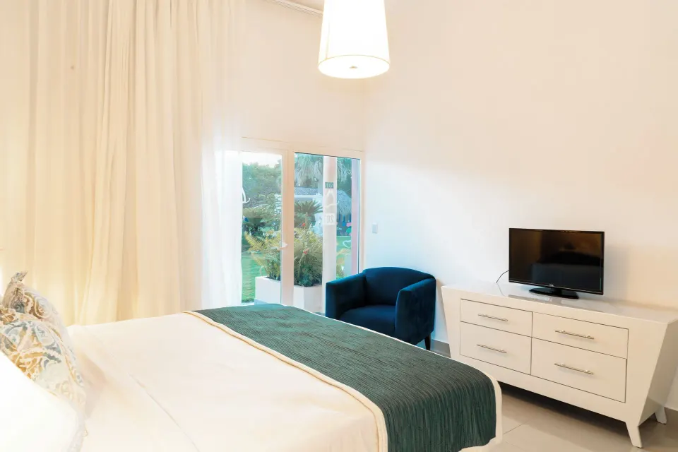 Family Suite king bed with TV dresser and blue chair at Hodelpa Garden Suites Golf & Convention Center.