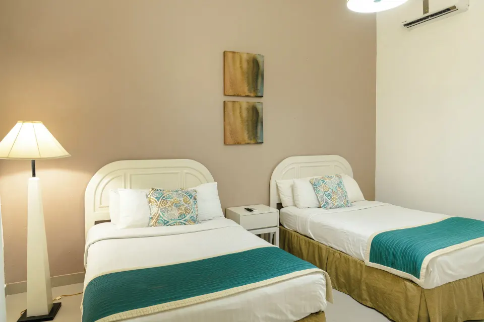 Family Suite bedroom with two beds and teal runners at Hodelpa Garden Suites Golf & Convention Center.